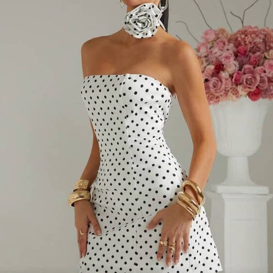 Woman wearing a strapless polka dot dress with floral accessories against a neutral background